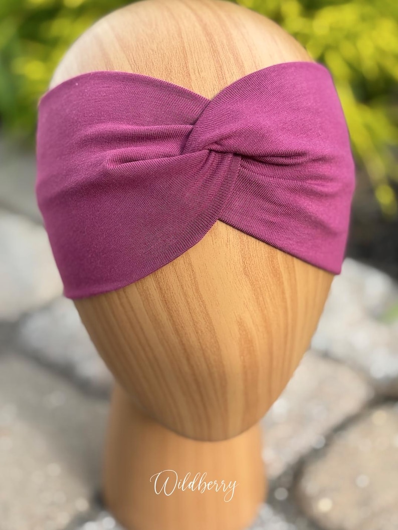 May include: A deep magenta-colored headband with a twisted knot design. The headband is displayed on a wooden head form. The word "Wildberry" is written in cursive script at the bottom of the image.