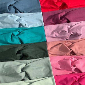 May include: A collection of colorful headbands in various shades, including navy, teal, red, and pink. Each headband features a twisted knot design, showcasing a range of solid colors. The headbands are made of soft fabric.