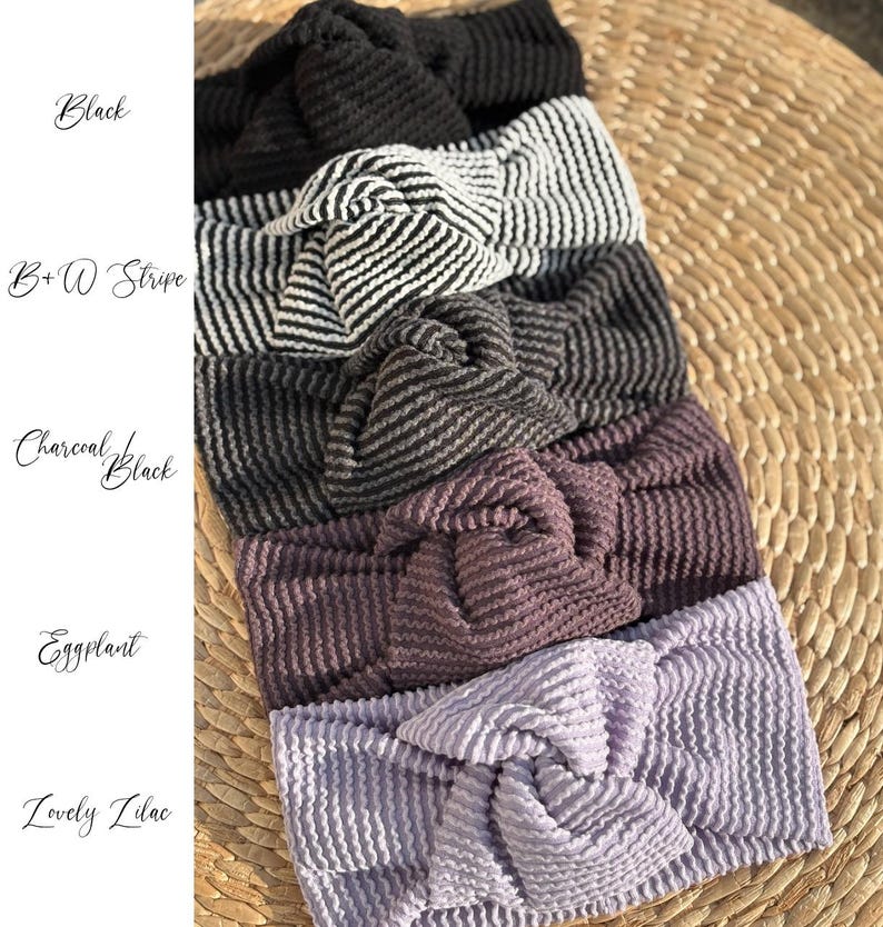Pu&ograve; includere: Una collezione di fasce per capelli annodate in vari colori, tra cui nero, a righe bianche e nere, nero antracite, melanzana e lilla. Le fasce sono realizzate in tessuto strutturato e sono disposte su una superficie intrecciata. I nomi dei colori sono scritti in corsivo.