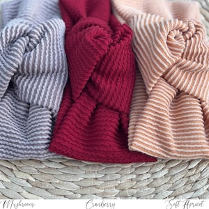 Pu&ograve; includere: Primo piano di tre fasce annodate nei toni del grigio, rosso mirtillo e albicocca chiaro. Le fasce hanno un design strutturato e a coste. I nomi "Mushroom", "Cranberry" e "Soft Apricot" sono scritti sotto.
