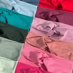 May include: A collection of colorful headbands in various shades, including teal, pink, red, and green. The headbands are made of soft fabric and feature a twisted knot design. The assortment showcases a range of colors, from light pastels to vibrant hues.