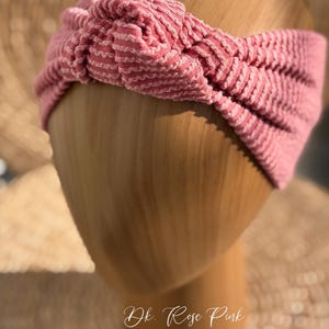 Pu&ograve; includere: Una fascia annodata rosa scuro con un design a coste strutturato. La fascia &egrave; esposta su una forma di testa in legno. Il testo "Dk. Rose Pink" &egrave; scritto in corsivo in basso nell'immagine.