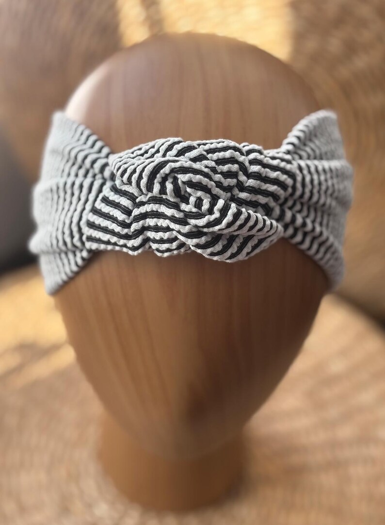 K&ouml;nnte beinhalten: Ein gestreiftes Turban-Haarband in Schwarz und Wei&szlig; mit einem Knotendesign.