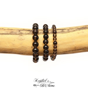 Peut inclure: Trois bracelets en quartz fumé brun de tailles différentes, empilés sur une branche de bois.