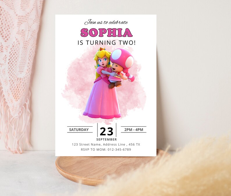 Puede incluir: Una invitaci&oacute;n de cumplea&ntilde;os rosa y blanca con una imagen de dibujos animados de la princesa Peach y Toad de la serie de videojuegos Super Mario Bros. La invitaci&oacute;n dice "&iexcl;&Uacute;nete a nosotros para celebrar que Sophia cumple dos a&ntilde;os!" e incluye la fecha, la hora y la informaci&oacute;n de RSVP.
