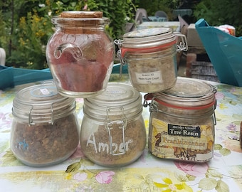 May include: Five glass jars with lids containing different types of tree resin. The jars are labeled "Amber", "Tree Resin Frankincense", and "Resin-02 Red Gum Copal 250g".
