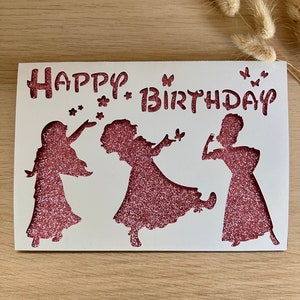 May include: A white card with the words "Happy Birthday" in pink glitter lettering. Three pink glitter silhouettes of girls are cut out of the card, with butterflies surrounding them.