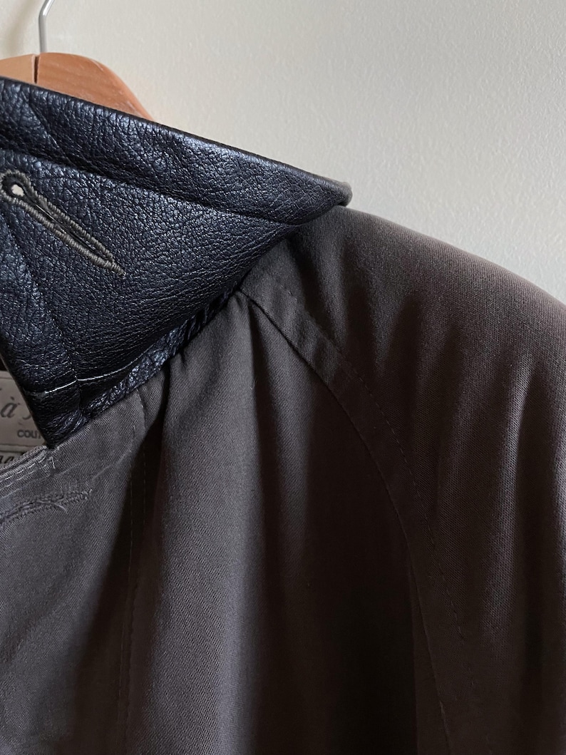 Puede incluir: Una chaqueta gris oscuro con cuello de cuero negro. El cuello tiene un detalle cosido.