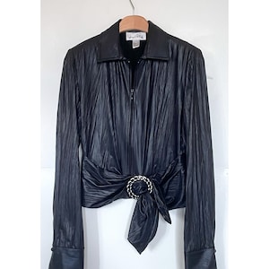 May include: A black long-sleeved shirt with a zip fastening and a tie at the waist. The shirt has a silver buckle on the tie.