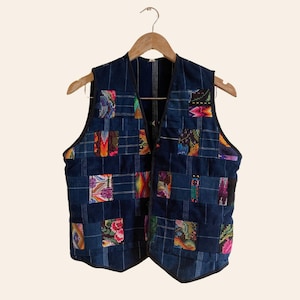 May include: A blue quilted vest with a patchwork design featuring colorful squares. The vest has a zipper closure and a V-neck.