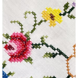 Peut inclure: Tissu blanc avec un motif de point de croix représentant des fleurs roses, rouges, jaunes, vertes et orange. Les fleurs sont reliées par des vignes vertes.