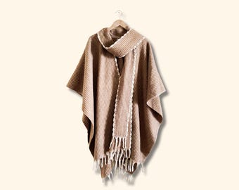 May include: A brown striped poncho with a white fringe trim and a matching white scarf. The poncho is hanging on a wooden hanger.