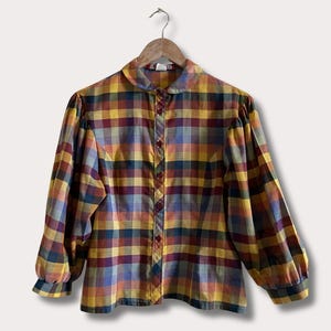 May include: A long-sleeved button-down shirt with a plaid pattern in shades of yellow, burgundy, blue, and orange. The shirt has a rounded collar and is hanging on a wooden hanger.