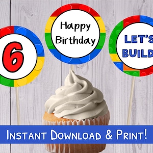 Puede incluir: Tres adornos para cupcakes coloridos con temática de Lego. Los adornos muestran las palabras "Feliz cumpleaños", "¡Vamos a construir!" y el número "6".