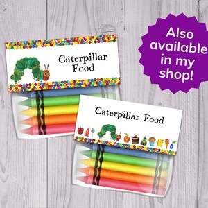 May include: A set of two clear plastic containers with colourful crayons inside. The containers have labels that say "Caterpillar Food". One label features a green caterpillar with a red head and the other label features a green caterpillar with a red head and a variety of colourful foods.