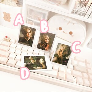 May include: Four white photo frames with black borders, each featuring a different character from a video game. The frames are arranged on a white keyboard with pink keys.