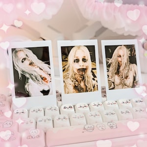 May include: Three polaroid-style photos featuring a person with pale skin, long blonde hair, and dark makeup, with blood-like stains. The photos are displayed on a keyboard with white and pink keycaps.