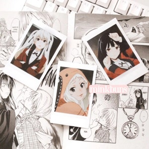 May include: Three instant photo prints featuring anime characters. The first print shows a girl with long, dark hair wearing a red and black outfit. The second print shows a girl with long, blonde hair wearing a red and white hooded jacket. The third print shows a girl with long, black hair wearing a red and black outfit. The prints are arranged on a table with a manga book.