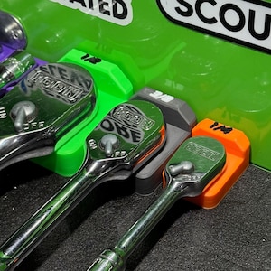 May include: A close-up shot of a set of chrome ratchets with green, gray, and orange holders. The ratchets are labeled with the text "SCOUT" and "ELEVATED". The image shows a variety of sizes, including 1/4, 3/8, and 1/2 inch.