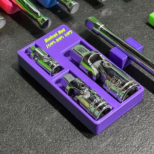May include: A purple plastic storage tray containing three chrome swivel socket adapters of varying sizes. The tray features the text Swivel Set 1/4", 3/8", 1/2" printed in yellow. The metal tools are arranged in custom-fitted slots within the tray.