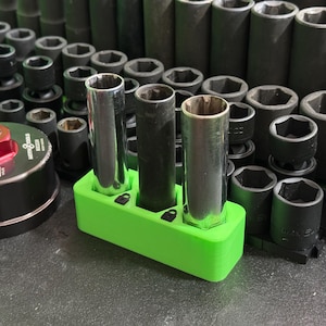 May include: A collection of automotive tools, including sockets and a filter wrench. Three metal sockets are held in a bright green holder. The background is filled with various sizes of black sockets, suggesting a mechanic's workspace.