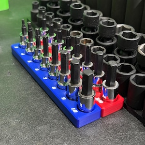 May include: A set of hex bit sockets arranged on blue and red plastic organizers. The sockets feature chrome-plated bases with black hexagonal tips. The blue organizer is clearly marked with white numbers ranging from 3 to 10 for size identification.