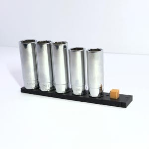 May include: A set of five silver socket wrenches in a black holder with a small brown block on the right side.
