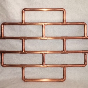 May include: A copper pipe wall shelf with a geometric design. The shelf has five horizontal sections and is made of copper pipe.