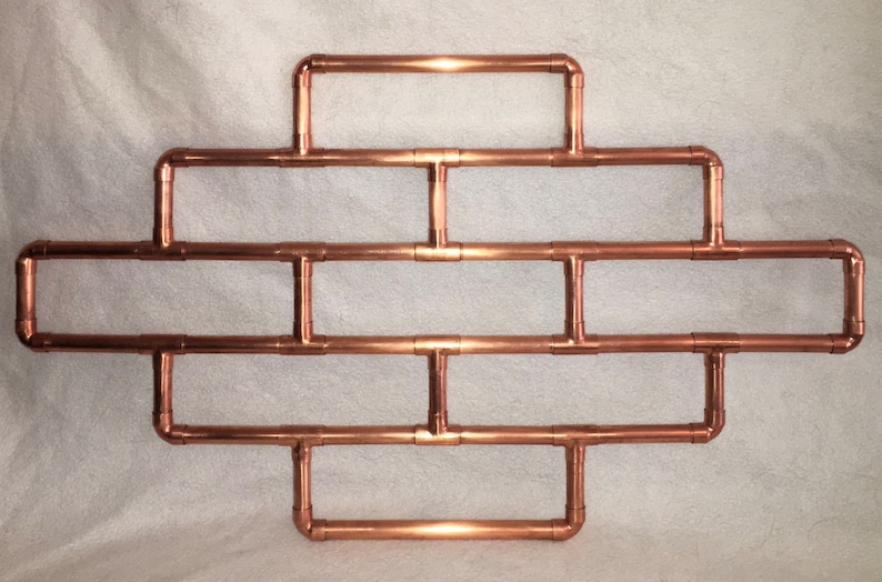 May include: A copper pipe wall shelf with a geometric design. The shelf has five horizontal sections and is made of copper pipe.
