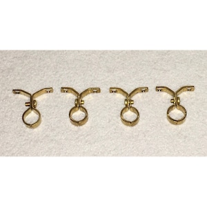 May include: Four gold metal pipe brackets with a round opening and a curved arm. The brackets are designed to hold pipes or rods.