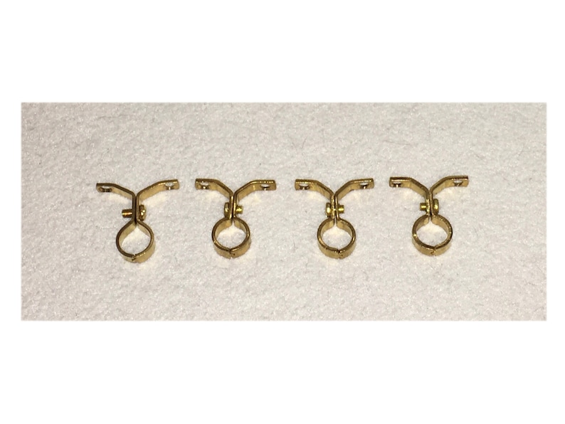 May include: Four gold metal pipe brackets with a round opening and a curved arm. The brackets are designed to hold pipes or rods.