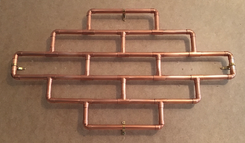 May include: A copper pipe wall shelf with a geometric design. The shelf is made of copper pipes and fittings and has a rustic industrial look.