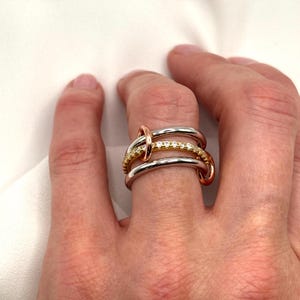 May include: A gold, silver, and rose gold ring with a row of small diamonds. The ring is made of three bands that are intertwined.