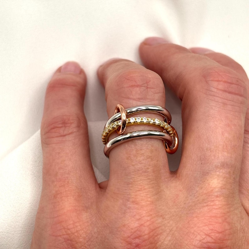 May include: A gold, silver, and rose gold ring with a row of small diamonds. The ring is made of three bands that are intertwined.