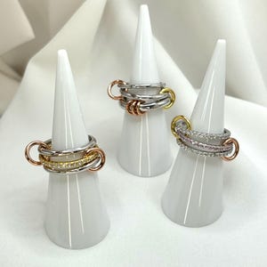 May include: Three silver rings with different colored accents. The first ring has a rose gold accent, the second ring has a yellow gold accent, and the third ring has a row of small pink and white stones.