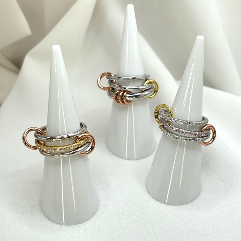 May include: Three silver rings with different colored accents. The first ring has a rose gold accent, the second ring has a yellow gold accent, and the third ring has a row of small pink and white stones.