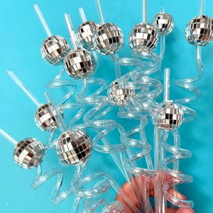May include: Clear plastic straws with a spiral design and small disco ball toppers. The disco balls are made of mirrored squares, reflecting light. The straws are arranged against a bright blue background.