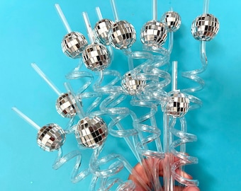 May include: Clear plastic straws with a spiral design and small disco ball toppers. The disco balls are made of mirrored squares, reflecting light. The straws are arranged against a bright blue background.