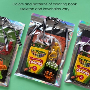 Puede incluir: Tres bolsas hologr&aacute;ficas que contienen sets de actividades de Halloween. Cada set incluye una caja de 8 crayones Crayola, un peque&ntilde;o esqueleto de pl&aacute;stico, un marco de pl&aacute;stico blanco y un juguete fidget de silicona, atados con una cinta a rayas.