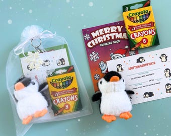 Puede incluir: Un set de regalo con dos juguetes de pingüino de peluche, dos cajas de ocho crayones Crayola, un libro para colorear Merry Christmas y un certificado de adopción. Un pingüino está dentro de una bolsa de organza blanca con un llavero de copo.