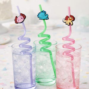 May include: Three spiral drinking straws in purple, green, and pink, each topped with a colorful axolotl character. The straws are placed inside three clear glasses filled with ice cubes, showcasing their distinct curly shapes and designs.
