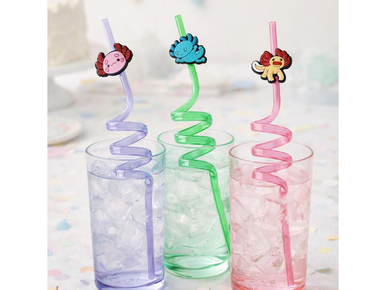 May include: Three spiral drinking straws in purple, green, and pink, each topped with a colorful axolotl character. The straws are placed inside three clear glasses filled with ice cubes, showcasing their distinct curly shapes and designs.
