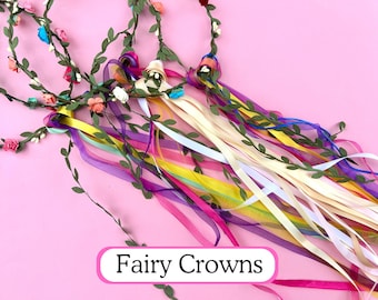 May include: Three fairy crowns with colorful ribbons and floral accents are displayed against a pink background. The crowns feature green vines, small flowers in various colors, and long, flowing ribbons in shades of yellow, pink, purple, and white. The text "Fairy Crowns" is in a pink oval.
