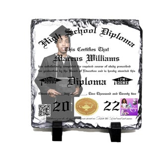 Puede incluir: Una placa de pizarra negra y blanca con un diseño de diploma de escuela secundaria. La placa presenta una foto de un graduado con toga y birrete, el texto "High School Diploma" y las palabras "This Certifies That Marcus Williams". La placa también incluye un icono de birrete de graduación, un sello y el año "2022".