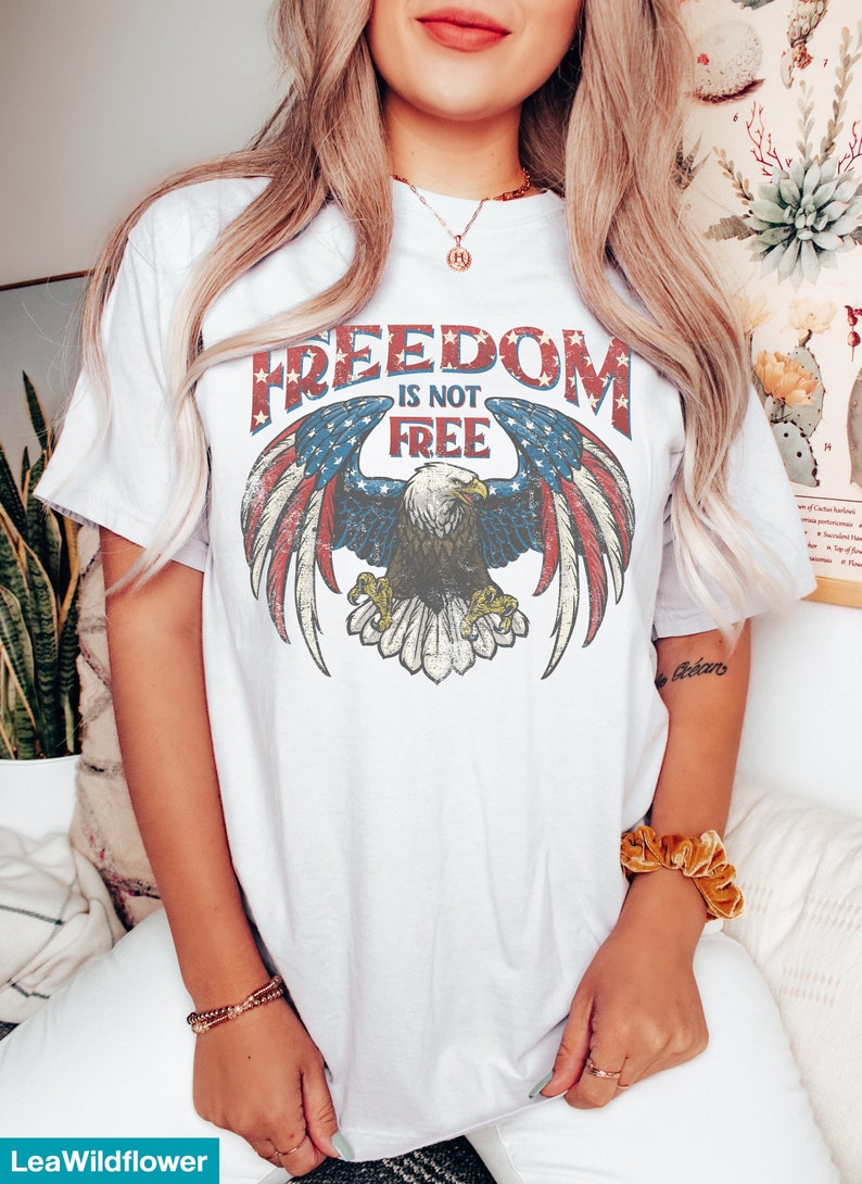 May include: White t-shirt with a vintage-style graphic of an eagle with American flag wings. The graphic says "Freedom is not free".