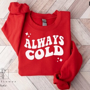 May include: Red sweatshirt with the text "ALWAYS COLD" in white retro font.