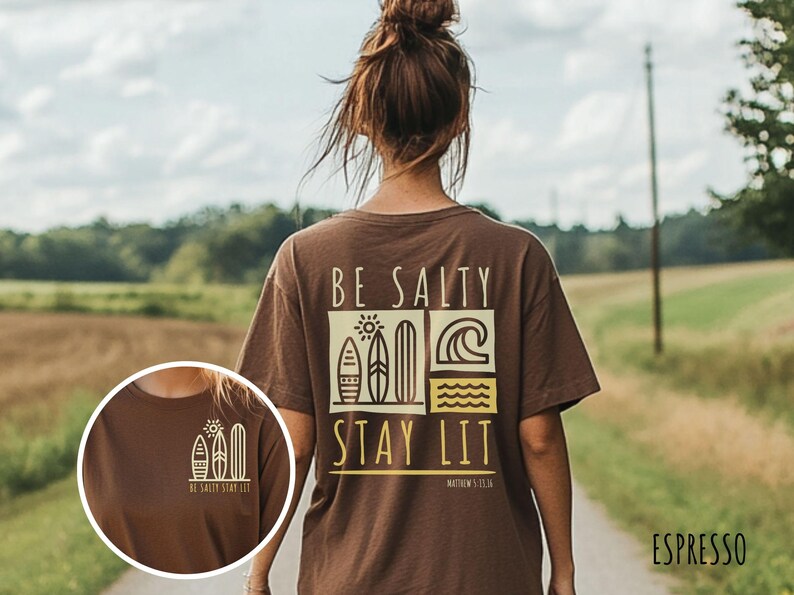 Może przedstawiać: Brązowa koszulka z graficznym wzorem desek surfingowych i tekstem "BE SALTY STAY LIT" w kolorze ż&oacute;łtym. Wz&oacute;r zawiera r&oacute;wnież tekst "MATTHEW 5:13".