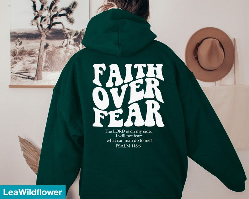 K&ouml;nnte beinhalten: Dunkelgr&uuml;ner Kapuzenpullover mit dem wei&szlig;en Schriftzug "FAITH OVER FEAR" auf der R&uuml;ckseite. Darunter steht ein Bibelvers: "Der HERR ist f&uuml;r mich, ich f&uuml;rchte mich nicht. Was k&ouml;nnen mir Menschen tun? PSALM 118,6."
