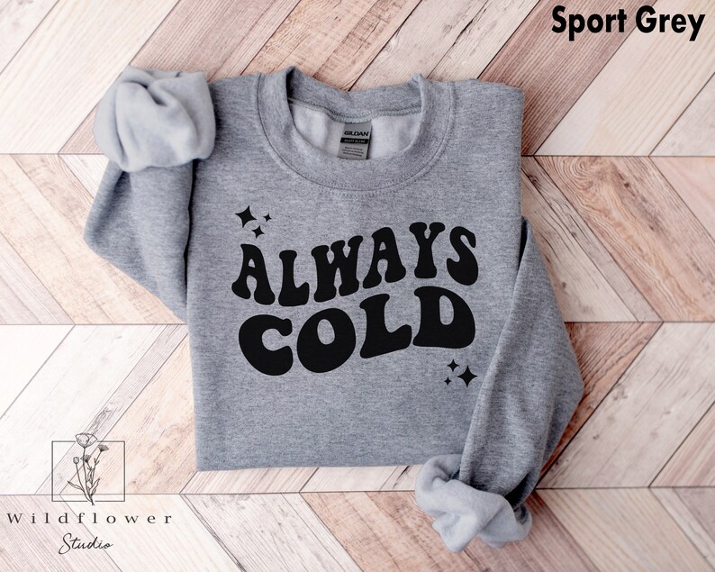 May include: A gray sweatshirt with the text "ALWAYS COLD" in a retro font. The text is in black and the sweatshirt is a sport gray color.