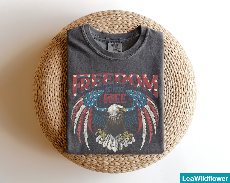 May include: A dark gray t-shirt with a vintage-style graphic of an eagle with American flag wings. The text "FREEDOM IS NOT FREE" is printed on the shirt.